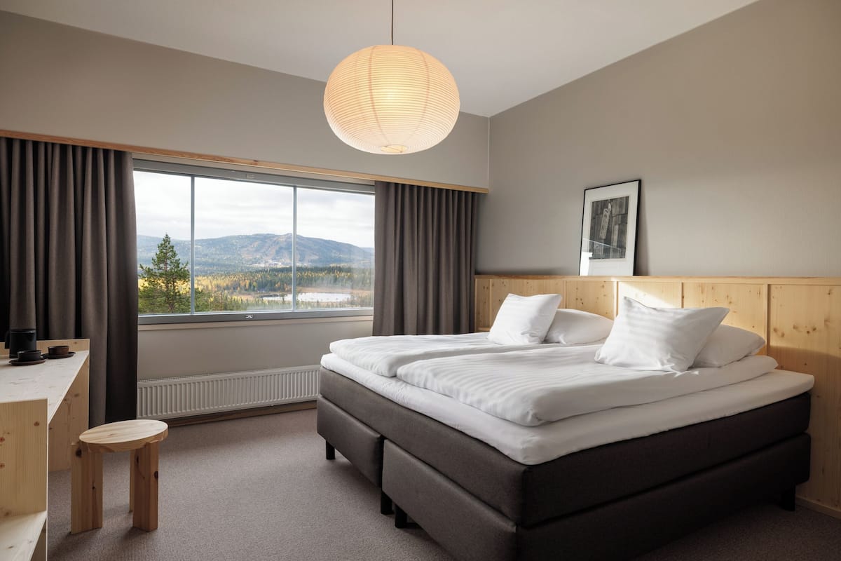 Une chambre avec un grand lit, un bureau, une chaise et une vue sur l’extérieur.