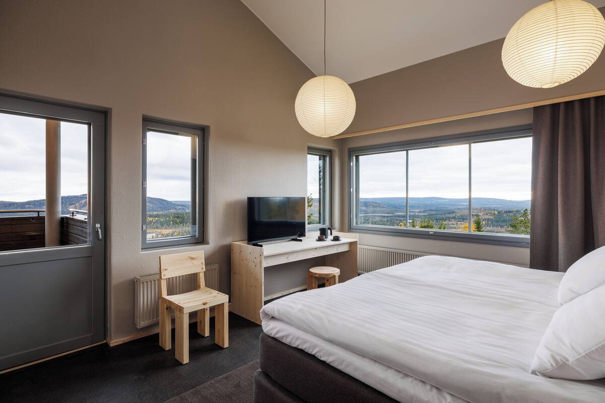 Une chambre d’hôtel moderne dotée d’un grand lit, d’un bureau avec une télévision et offrant une vue sur les montagnes grâce à de grandes fenêtres.