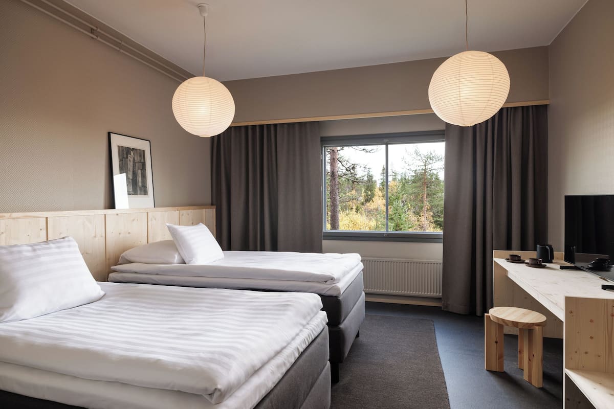 Une chambre d’hôtel avec deux lits, un bureau, une chaise et une grande fenêtre avec des rideaux.