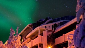 Un bâtiment enneigé, illuminé par une source de lumière vive au premier plan, entouré d’arbres chargés de neige.