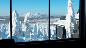 Une vue panoramique d’un paysage enneigé, avec une montagne en arrière-plan, un bâtiment dont le toit est recouvert de neige et des arbres également couverts de neige.