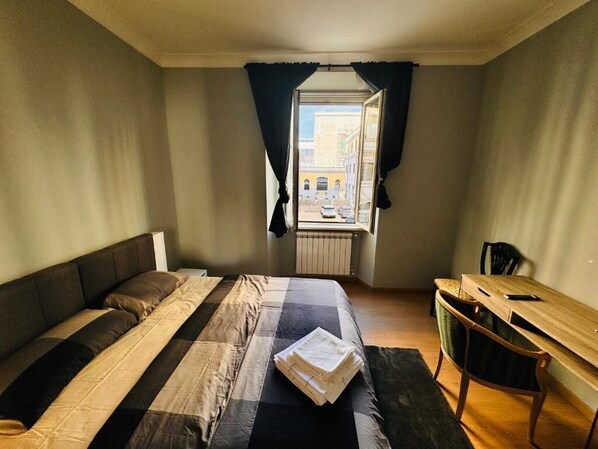 Un dormitorio con cama, escritorio y ventana con cortinas.