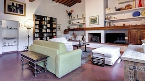 A living room with a sofa, a coffee table, a fireplace, a bookshelf, and a television. - Farinata Apartment by Mamo Florence (Florence)