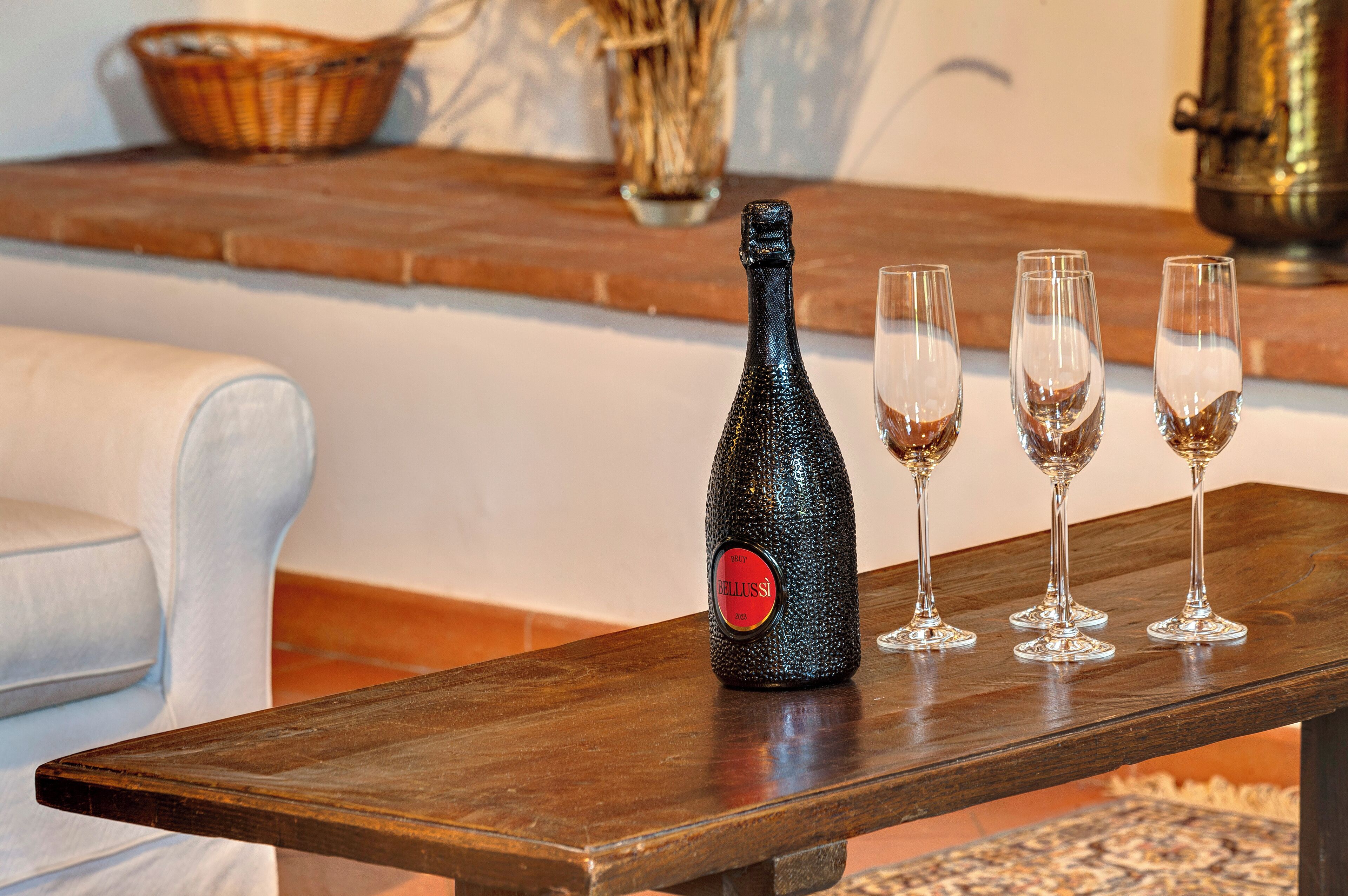 Een fles champagne en drie glazen op een houten tafel in een kamer met een witte bank en een schouw met bakstenen.