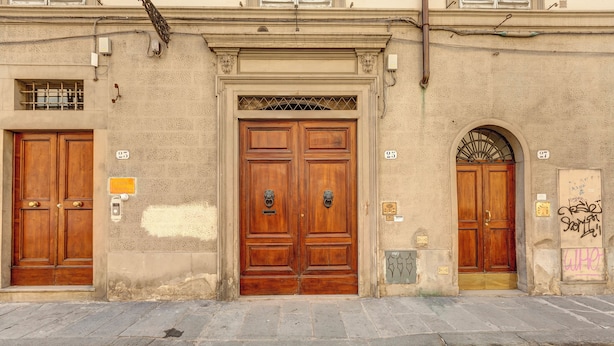 A building with two wooden doors, a stone-paved street, and a metal grate above the central door. - Farinata Apartment by Mamo Florence (Florence)