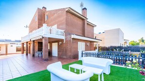 A two-story house with a balcony, a patio with outdoor furniture, and a fenced garden area.