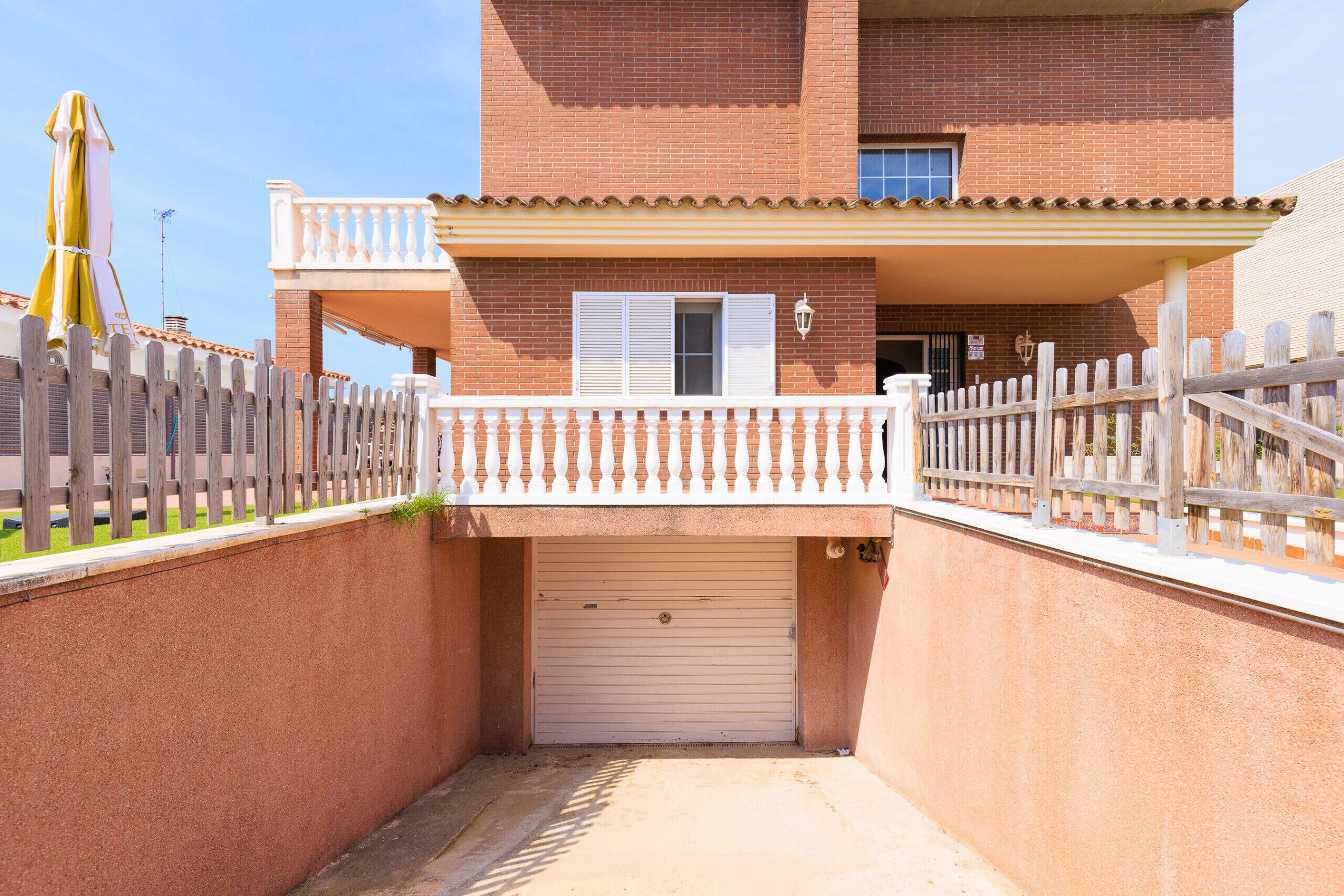A two-story building with a closed garage door, a balcony with a wooden railing, and a wooden fence surrounding the property.