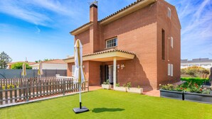 A brick house with a well-maintained lawn, a covered patio, and a wooden fence.