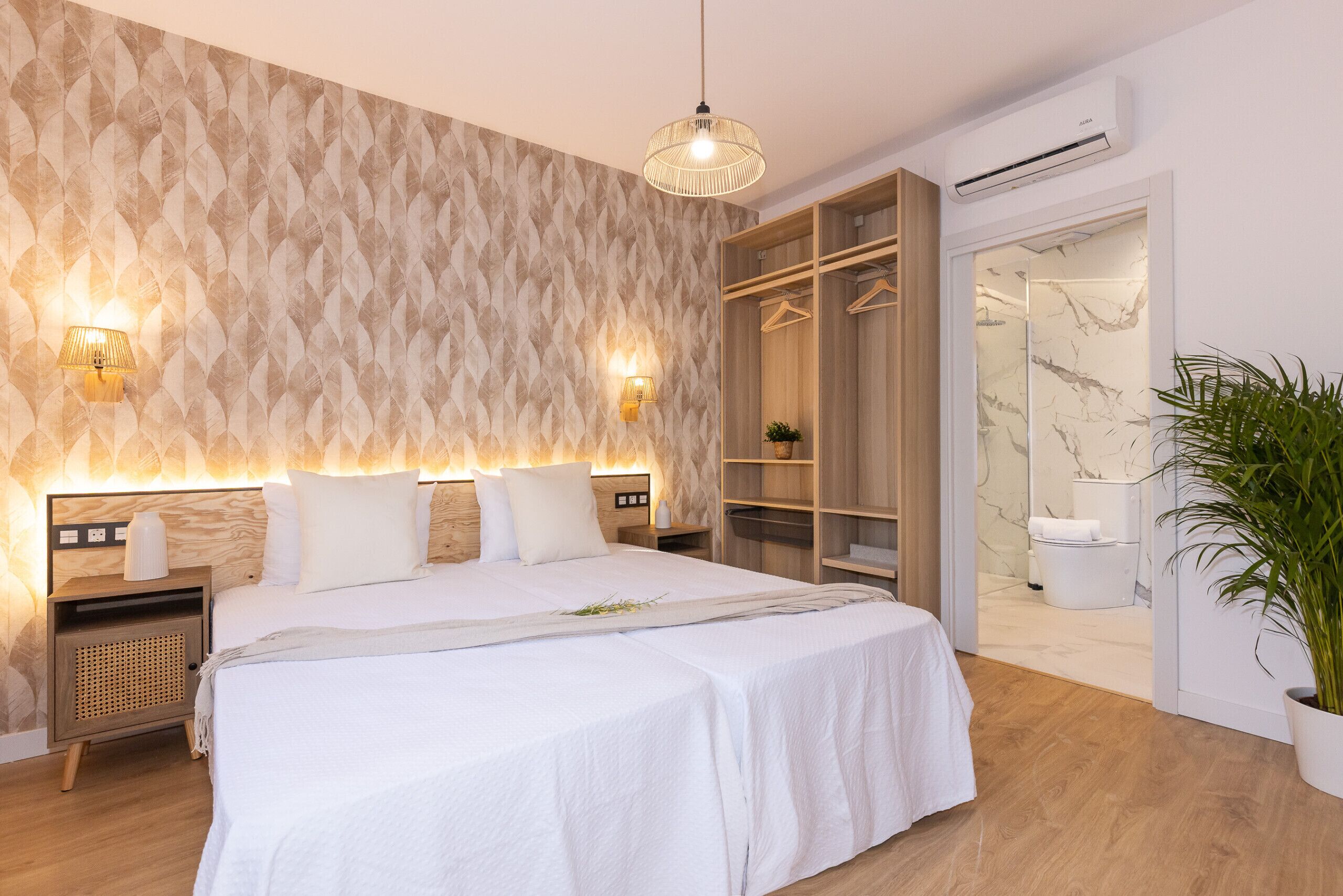 Een moderne slaapkamer met een groot bed, houten nachtkastjes, een kledingkast, en een zichtbare badkamer door een open deur.