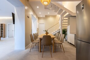A modern kitchen with a dining area, featuring a wooden table and chairs, a stainless steel refrigerator, and a staircase leading to an upper level. - Villa MORERA (Vila Seca)