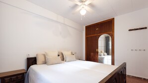 A bedroom with a large bed, wooden headboard, a ceiling fan, and a wooden wardrobe. - NAUTICO Apartment (Salou)