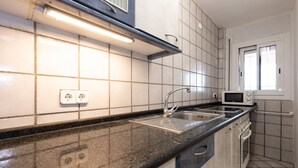 A kitchen with a black countertop, white tiled walls, a built-in oven, and a microwave. - NAUTICO Apartment (Salou)