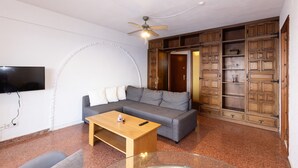 A living room with a grey sofa, a wooden coffee table, a ceiling fan, and built-in wooden cabinets. - NAUTICO Apartment (Salou)
