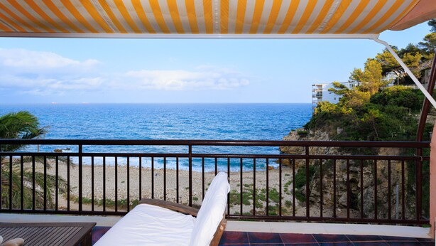 A balcony with a view of the sea, a wooden table, and a striped awning. - NAUTICO Apartment (Salou)