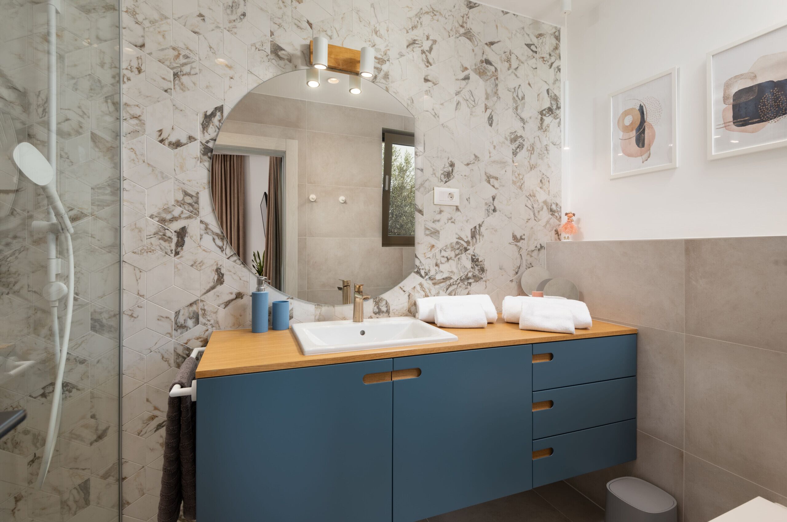 A modern bathroom with a marble backsplash, a wooden vanity, a large mirror, and a toilet.
