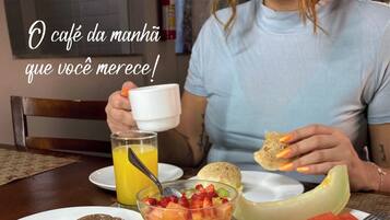 Mesa de café da manhã com diversos doces, um copo de suco de laranja e uma tábua de melancia.