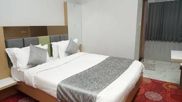 A neatly made bed with a grey and white patterned bedspread, a wooden headboard, and a red patterned rug.