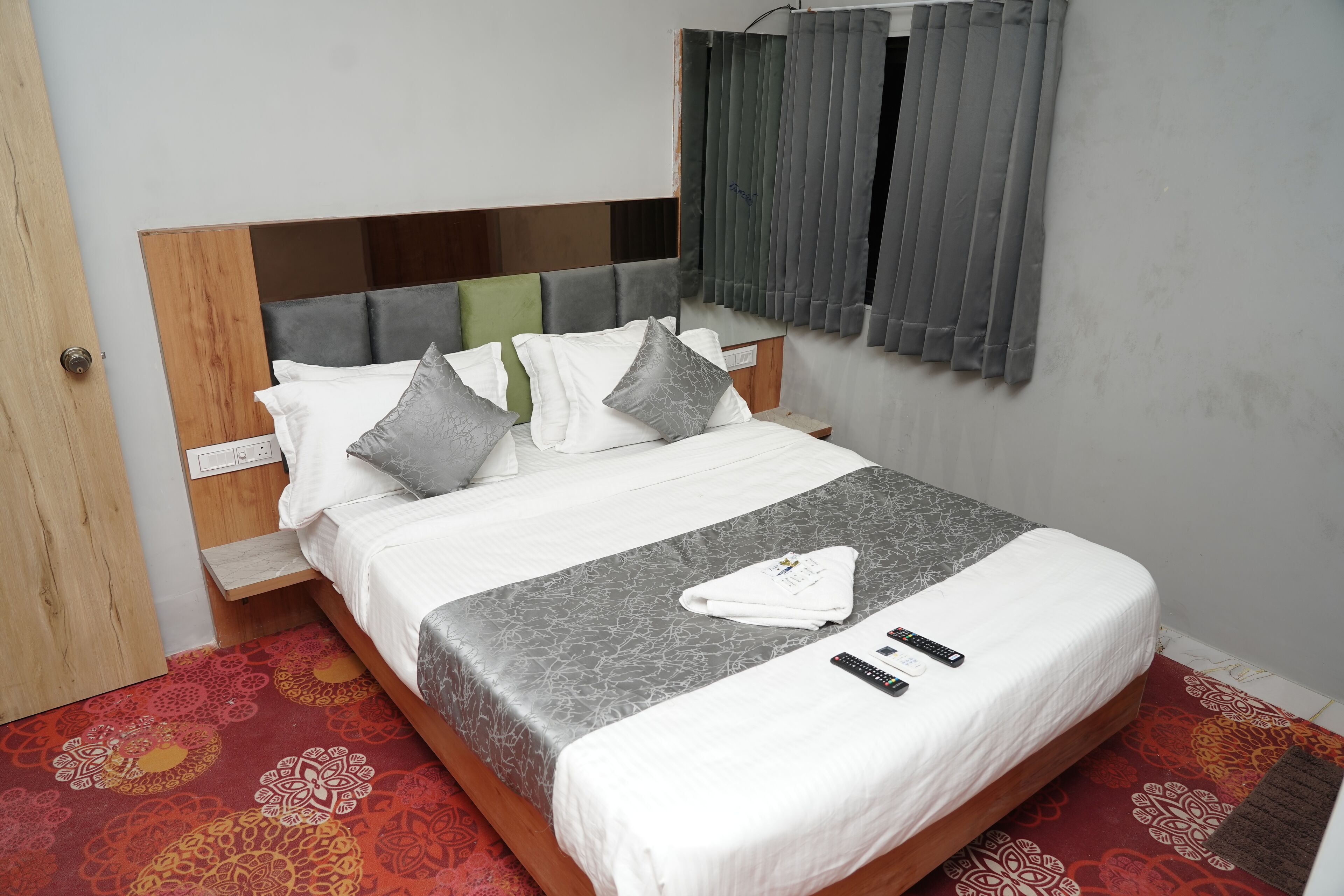 A neatly made bed with a grey patterned bedspread, white pillows, and a folded towel on the bed.