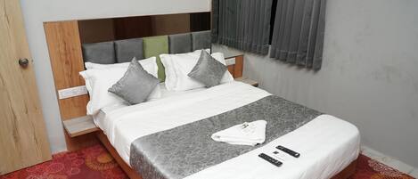 A neatly made bed with a grey patterned bedspread, white pillows, and a folded towel on the bed.