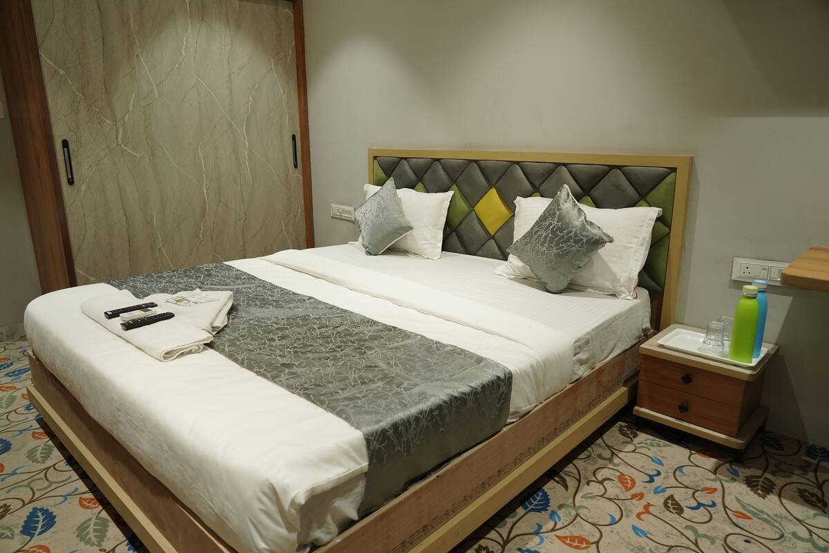 Una cama bien hecha con una colcha estampada, almohadas y una mesita de noche con una botella y vasos.
