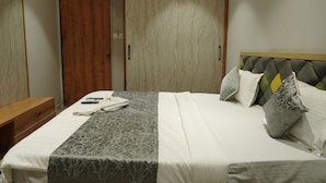 Un letto rifatto con cura, con una coperta grigia a motivi, un comodino in legno e un armadio dalla finitura simile al marmo.