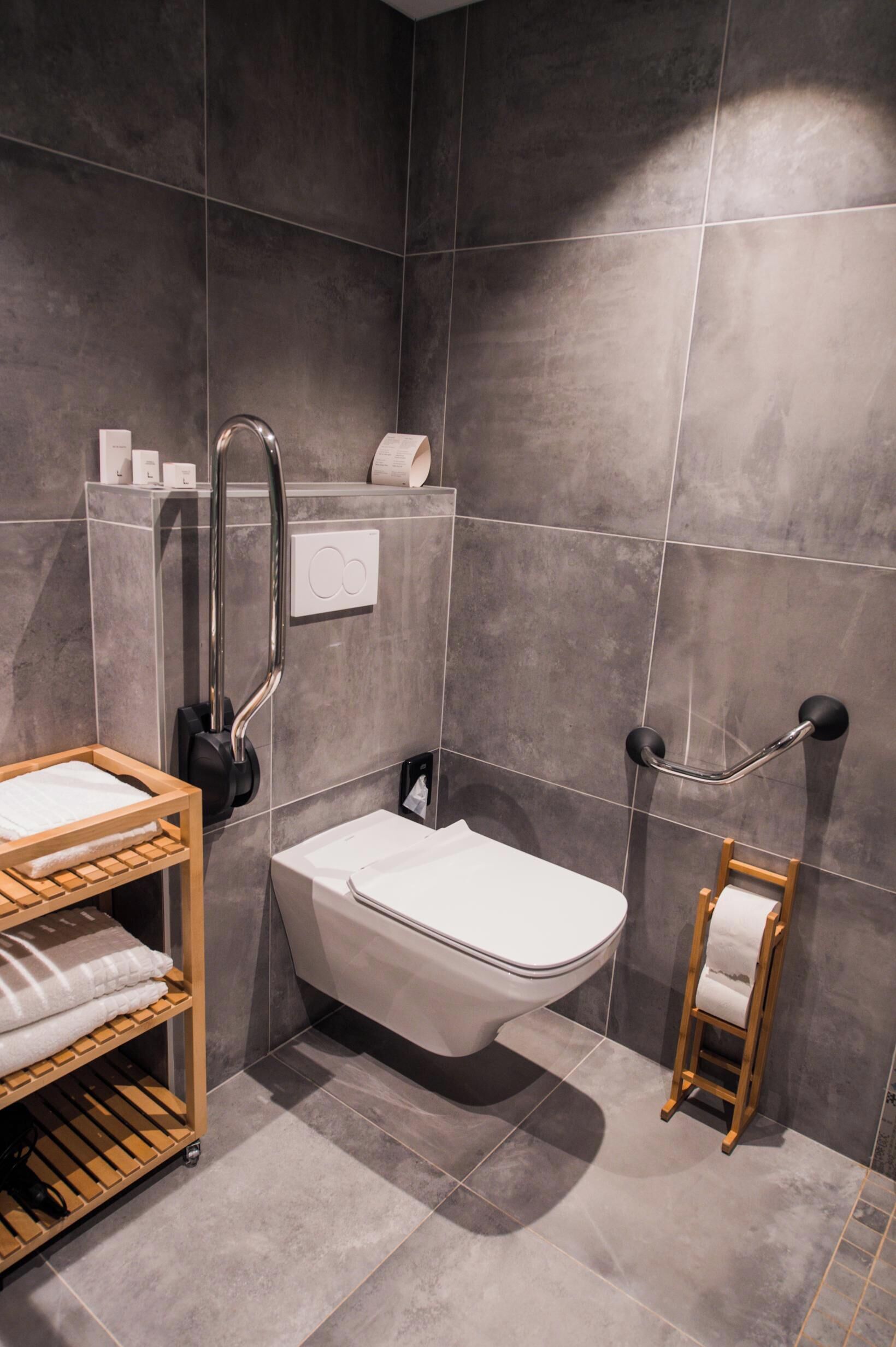 A modern bathroom with a shower, toilet, and a wooden shelf with towels.
