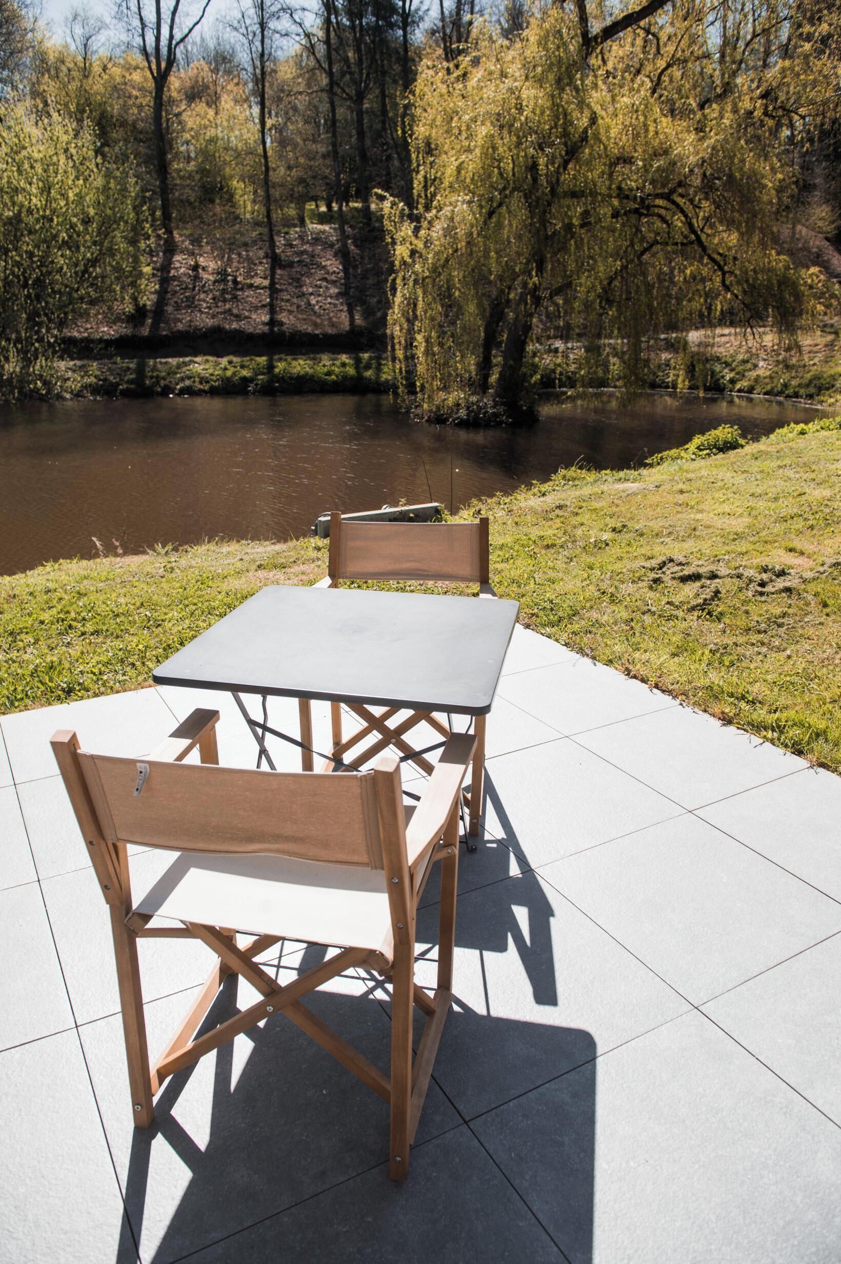 An outdoor table and chairs set on a tiled patio with a view of a river and trees.