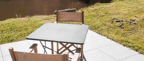An outdoor table and chairs set on a tiled patio with a view of a river and trees.