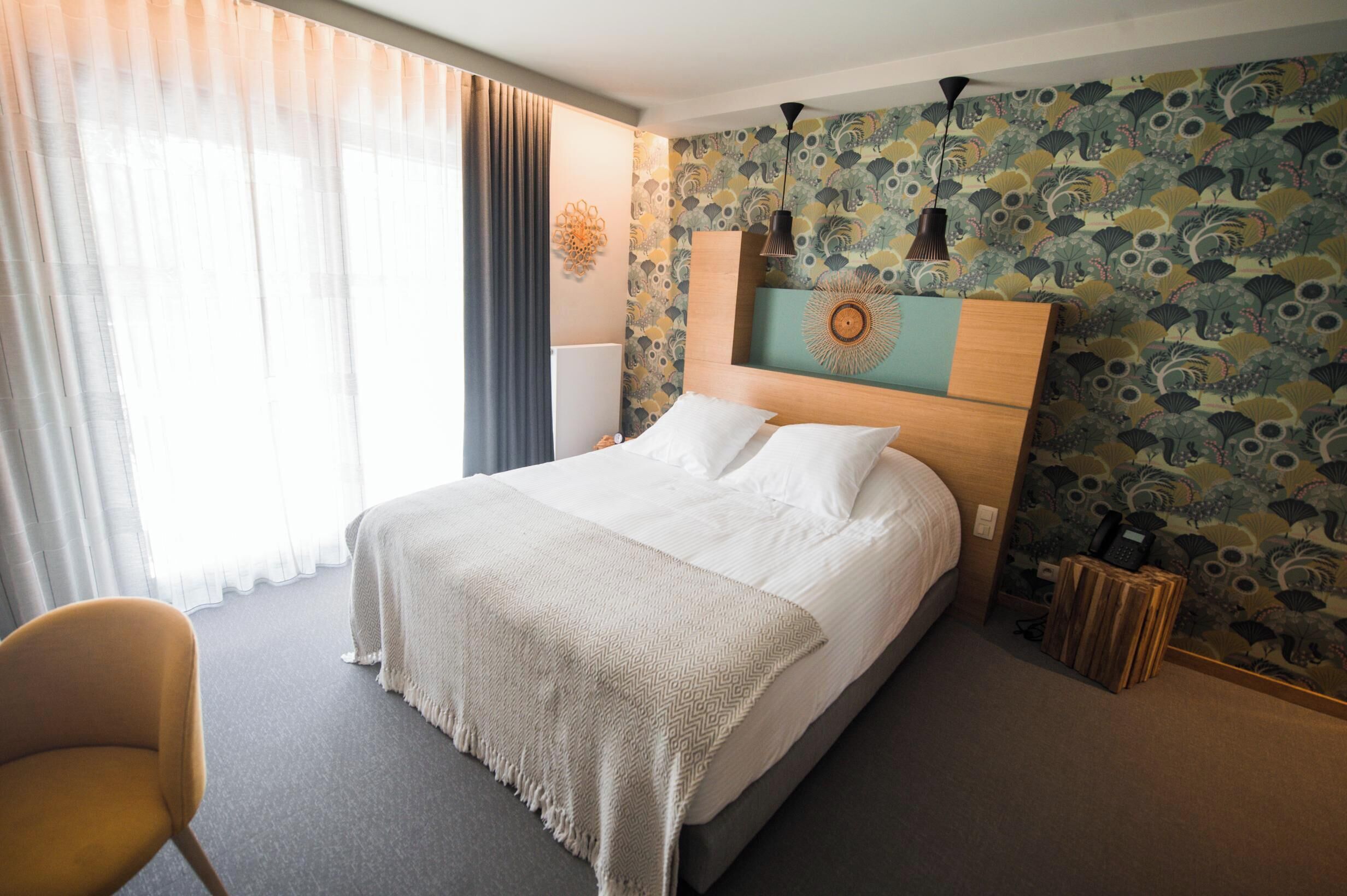 A hotel room with a large bed, a bedside table, a chair, and a decorative wall with a floral pattern.