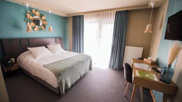 Habitación de hotel con cama, escritorio y silla. Hay un televisor, un teléfono y un florero con flores secas sobre el escritorio.