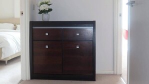 Un dormitorio con un armario de madera oscura, un espejo redondo y un jarrón con flores blancas en la pared.