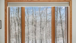 A window with a view of a forested area during winter. - Cozy Highridge Condo Unit I6 in Killington with pool and hot tub. (Killington)