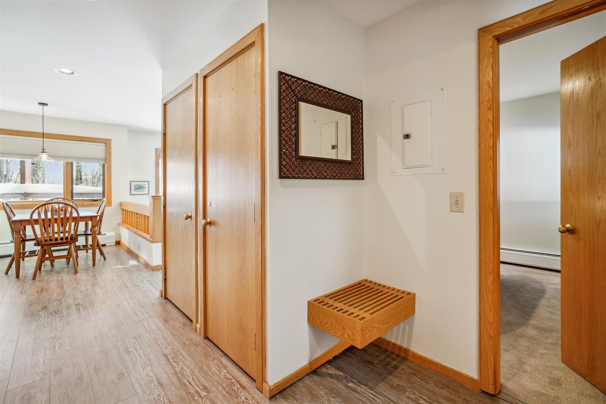A hallway with wooden flooring, a bench, a door, and a mirror on the wall.