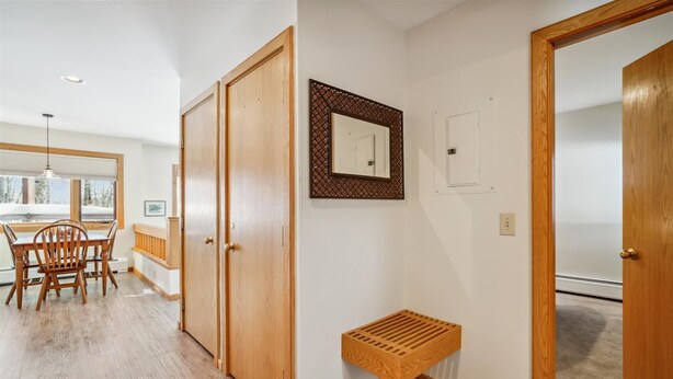 A hallway with wooden flooring, a bench, a door, and a mirror on the wall. - One-bedroom condo with pool, hot tub, weekend winter, shuttle, and EV charger (Killington)
