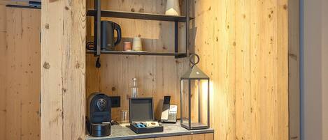 A wooden interior with a shelf holding a coffee maker, a lamp, and a small table with a laptop and a glass.
