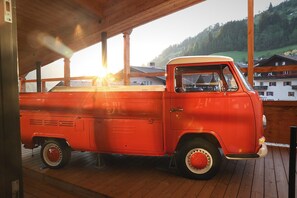A red vintage truck parked on a wooden deck with a view of houses and hills in the background. - La Tambra - Hotel Lodge (Santa Cristina Val Gardena)
