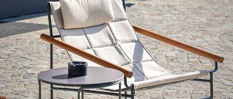 A lounge chair with a cushion and a small table, positioned in front of a building with a sign that reads 'LA TAMBRA'.