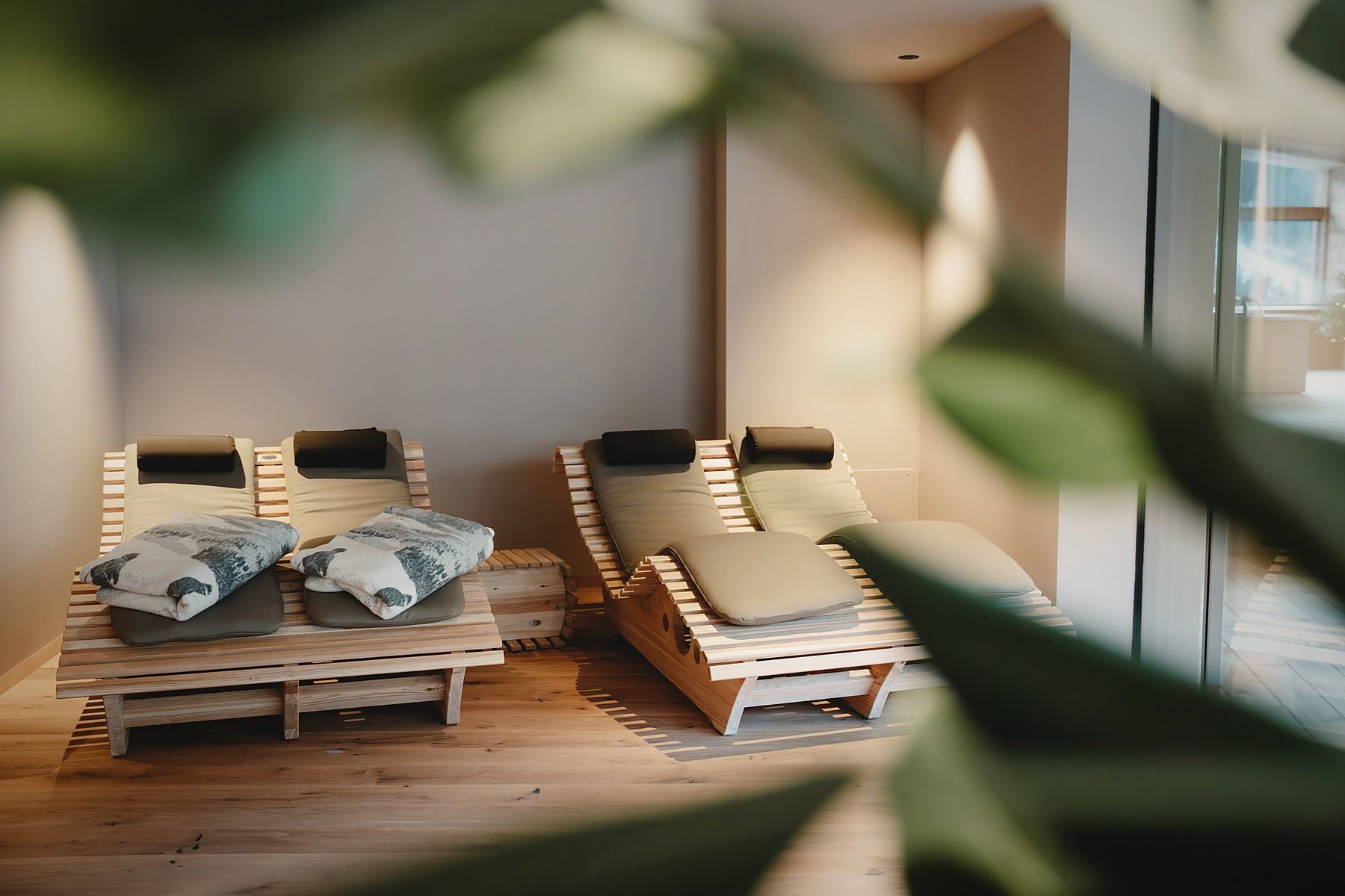 Zwei Holz-Loungestühle mit Kissen, platziert in einem Raum mit Holzboden und einem großen Fenster.