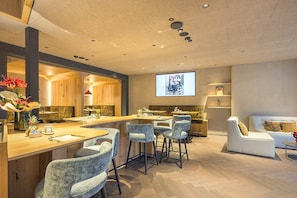 A modern bar area with bar stools, a counter, and a projection screen displaying a vintage car. - La Tambra - Hotel Lodge (Santa Cristina Val Gardena)