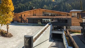 A modern hotel with a wooden facade, a sign reading 'HOTEL LODGE,' and a view of a mountainous landscape. - La Tambra - Hotel Lodge (Santa Cristina Val Gardena)