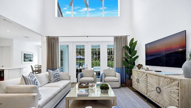 A spacious living room with a high ceiling, large windows, a flat-screen TV, and a modern coffee table.