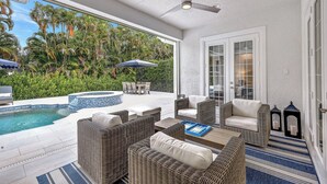 A sunlit patio with a pool, wicker furniture, and a ceiling fan.