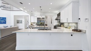 A modern kitchen with white cabinetry, a central island, and a dining area with a sofa and chairs.