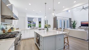 A modern kitchen with a central island, white cabinetry, and a dining area with wicker chairs.