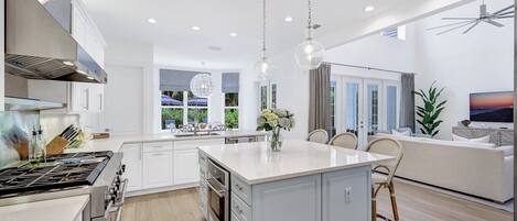 A modern kitchen with a central island, white cabinetry, and a dining area with wicker chairs.