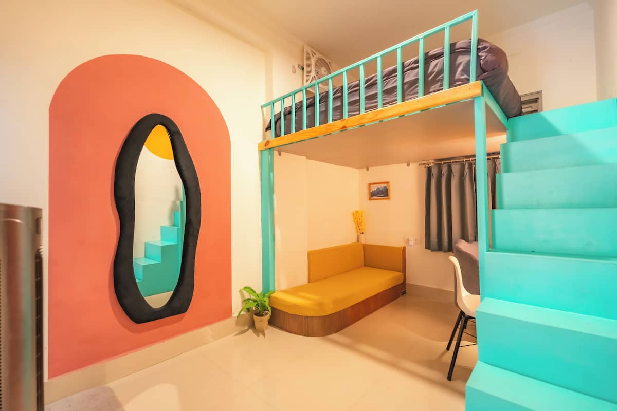 Une pièce comprenant un lit superposé, un canapé, une chaise, une plante en pot et un miroir fixé au mur.