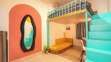 A room with a bunk bed, a sofa, a chair, a potted plant, and a wall-mounted mirror.