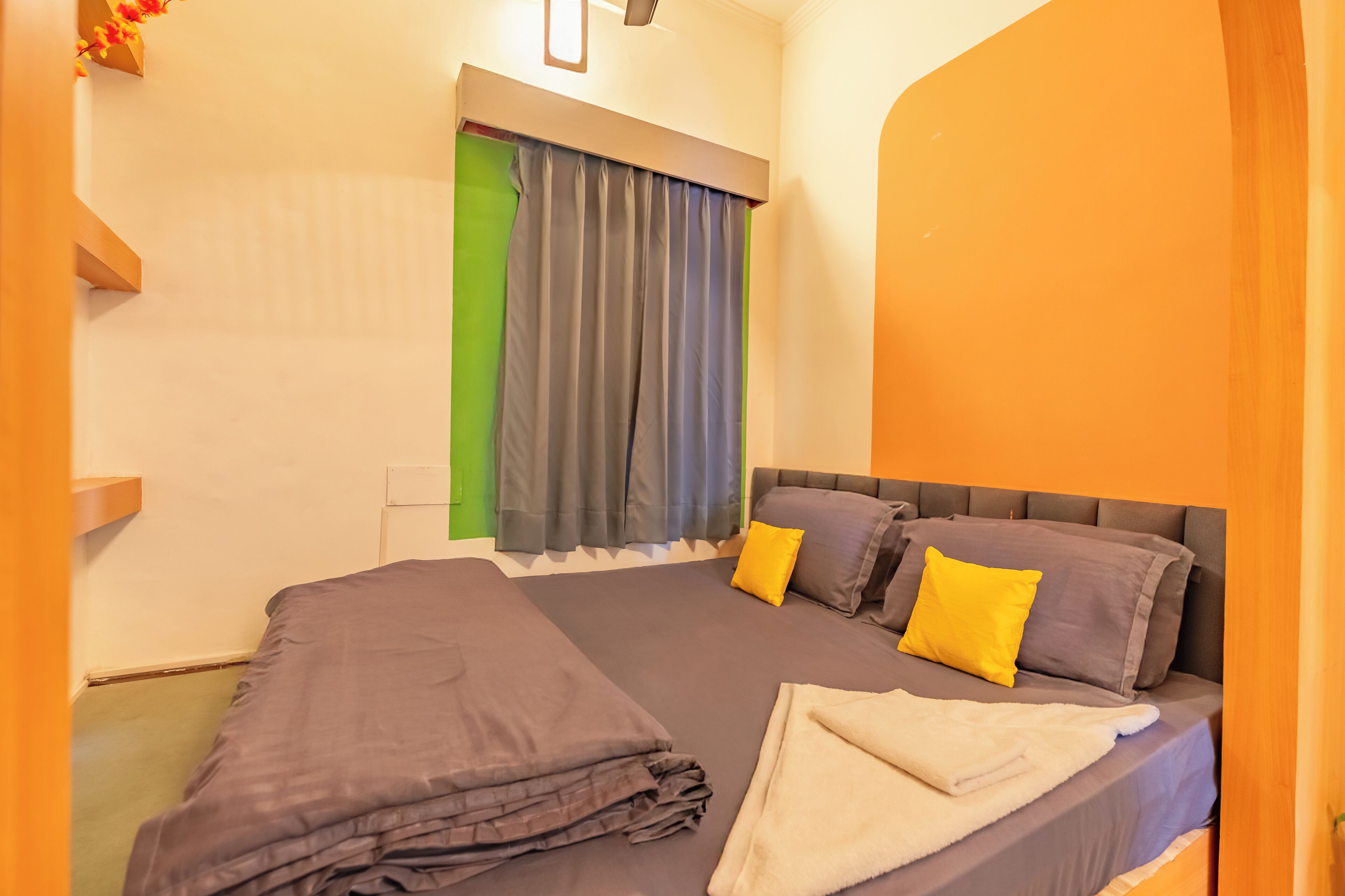 A neatly made bed with grey bedding and two yellow pillows, a grey headboard, and a window with grey curtains.