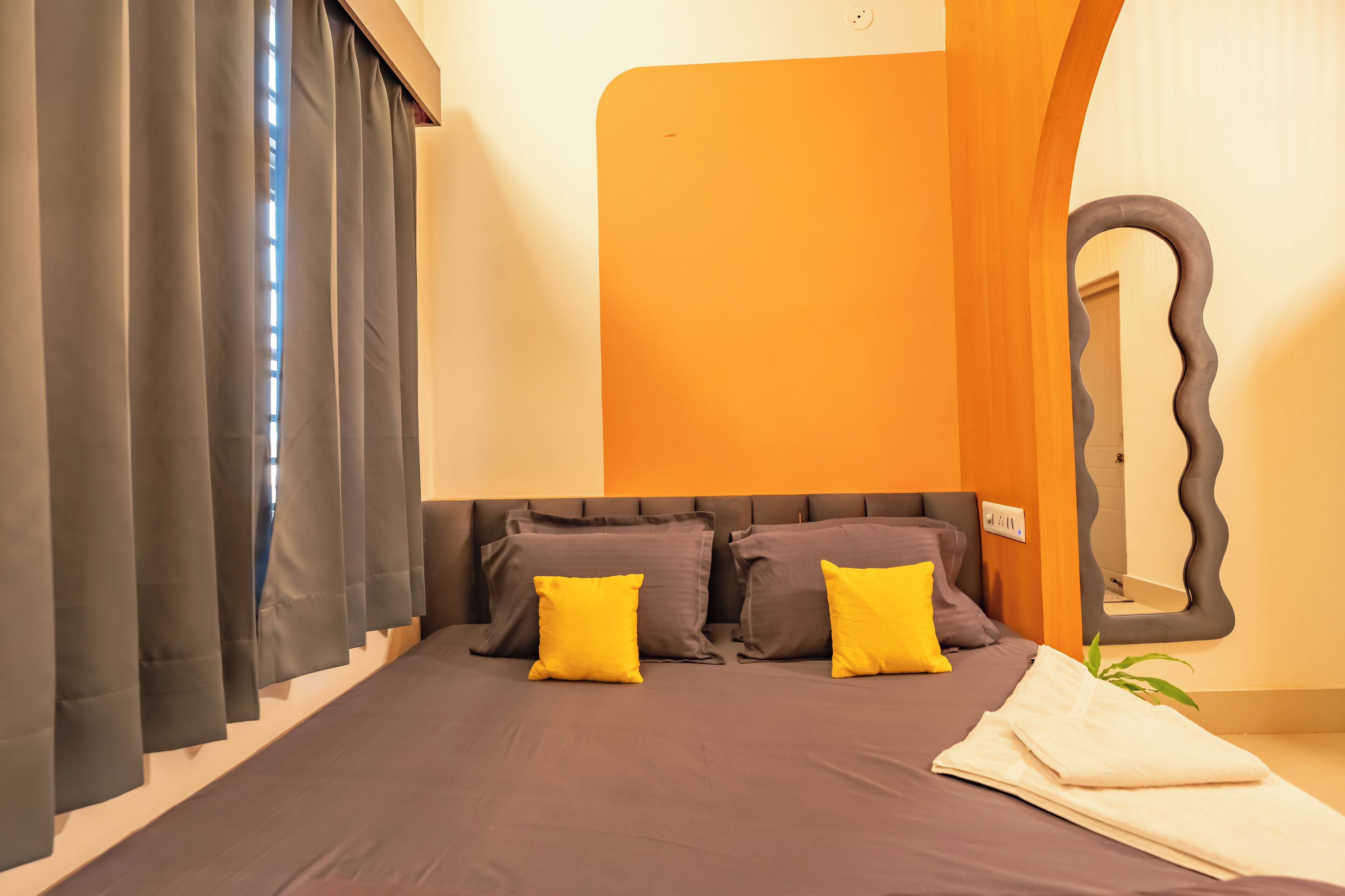A modern bedroom with a large bed, dark curtains, and a unique mirror design.