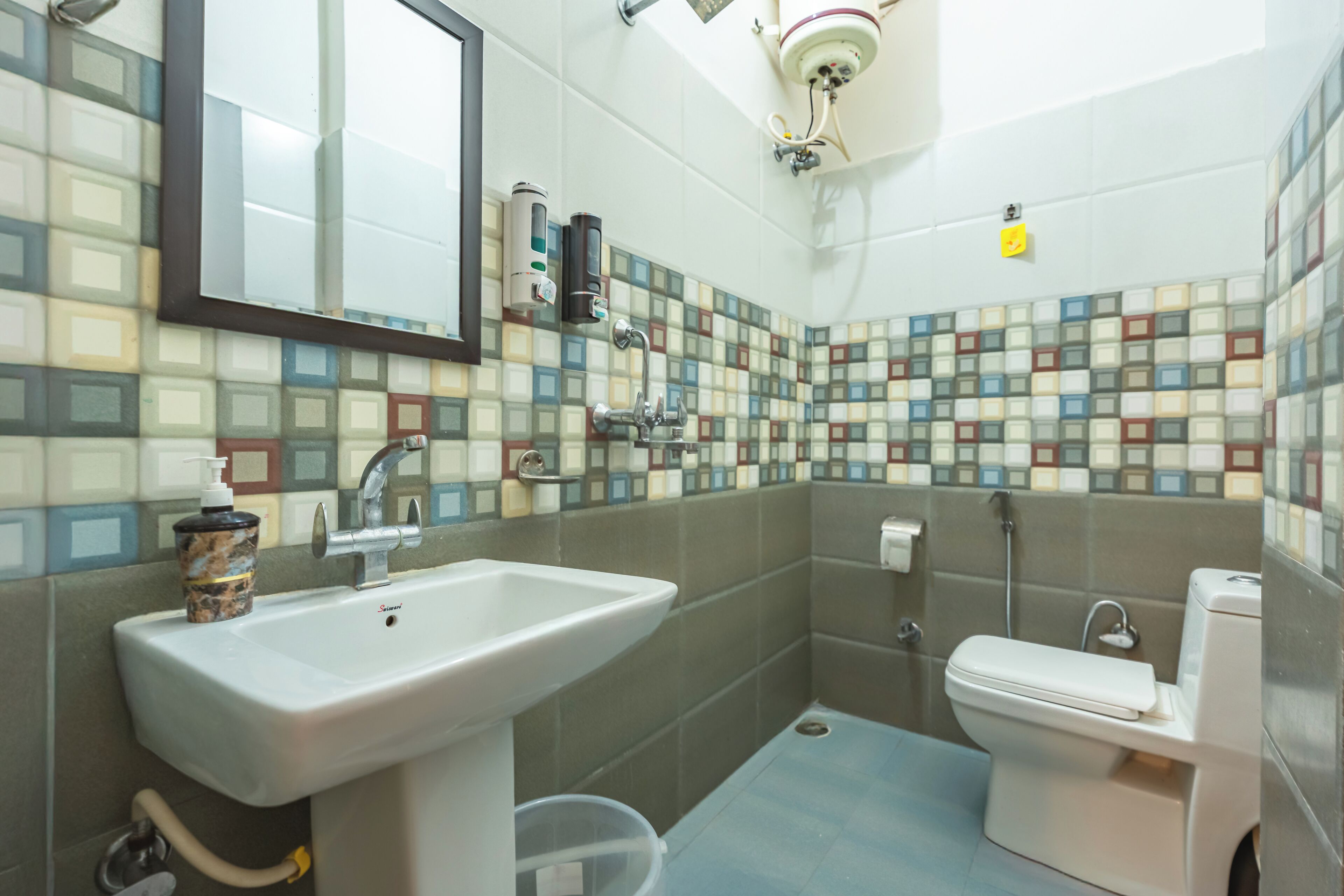 A bathroom with a sink, toilet, and a mirror. The walls are tiled with a mosaic pattern.